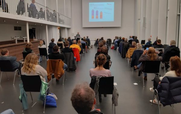 Viele Menschen sitzen in einem Saal und hören sich einen Vortrag an