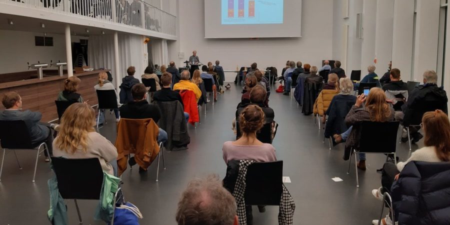 Viele Menschen sitzen in einem Saal und hören sich einen Vortrag an