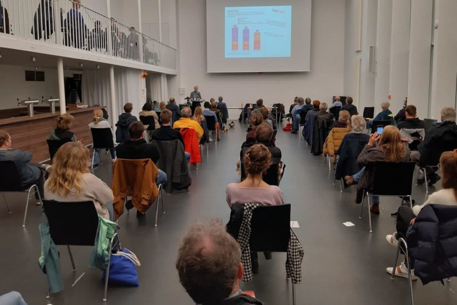 Viele Menschen sitzen in einem Saal und hören sich einen Vortrag an