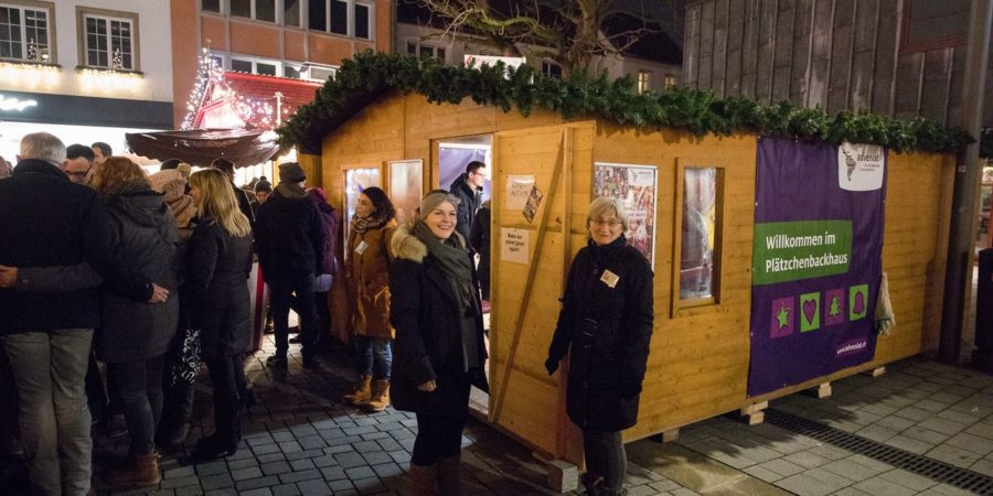 Ein Foto mit einem Weihnachnachts Stand aus Holz von adveniat (für die Menschen in Lateinamerika) und Menschen die davor stehen