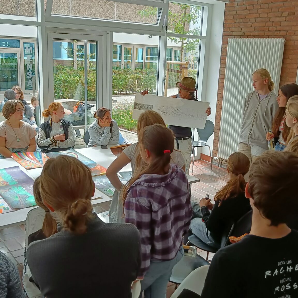 Viele Jugendliche sitzen um einen Tisch herum und schauen sich verschiedene Skizzen an