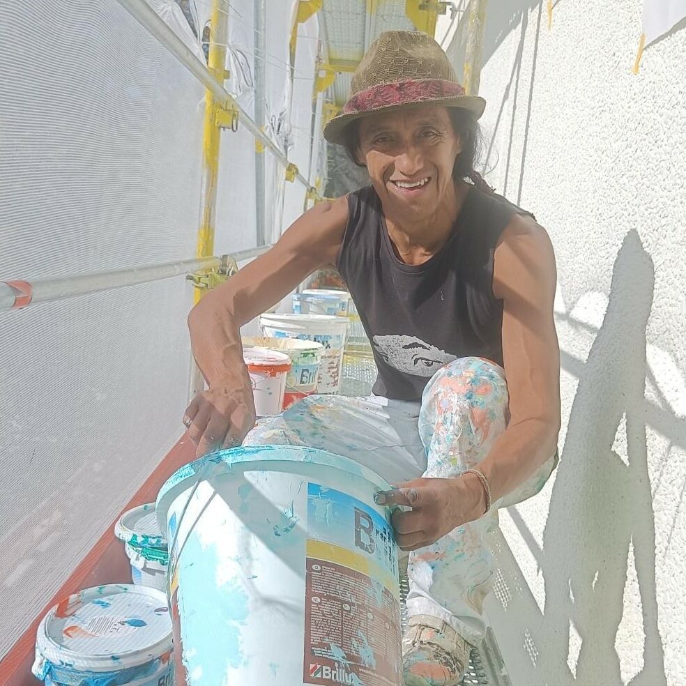 Der Künstler Jorge Hidalgo arbeitet an dem Wandbild am Ratsgymnasium. Er sitzt auf einem Gerüst und rührt in einem Farbeimer.