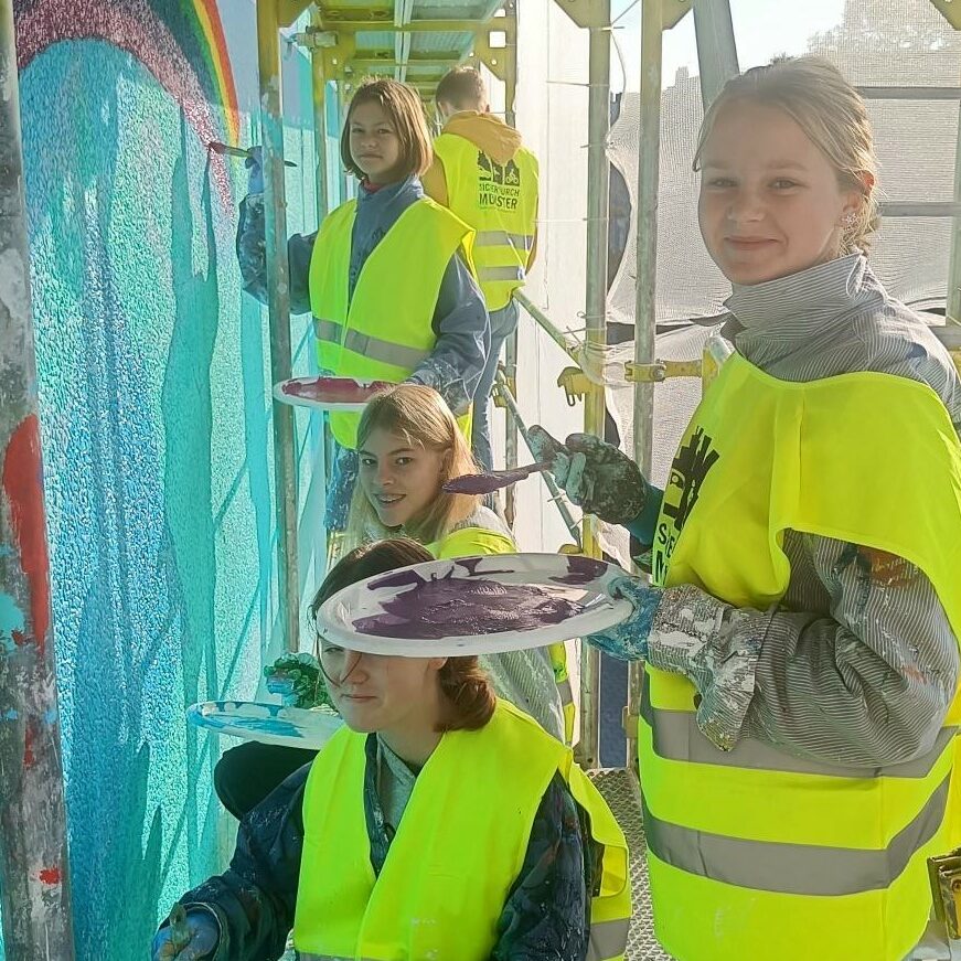 Schülerinnen des Ratsgymnasium sind am Malen an dem Wandbild am Ratsgymnasium
